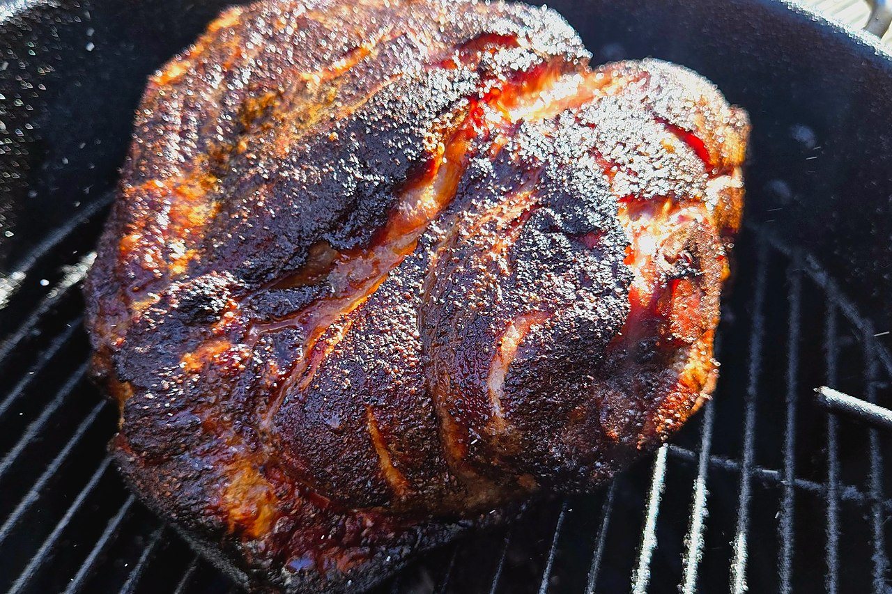 Smoked pork butt on the cooker with a dark exterior bark forming.