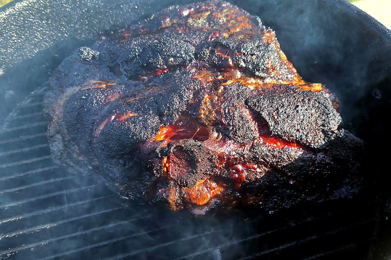 Pork butt in the smoker during the cook, showing bark development underway.