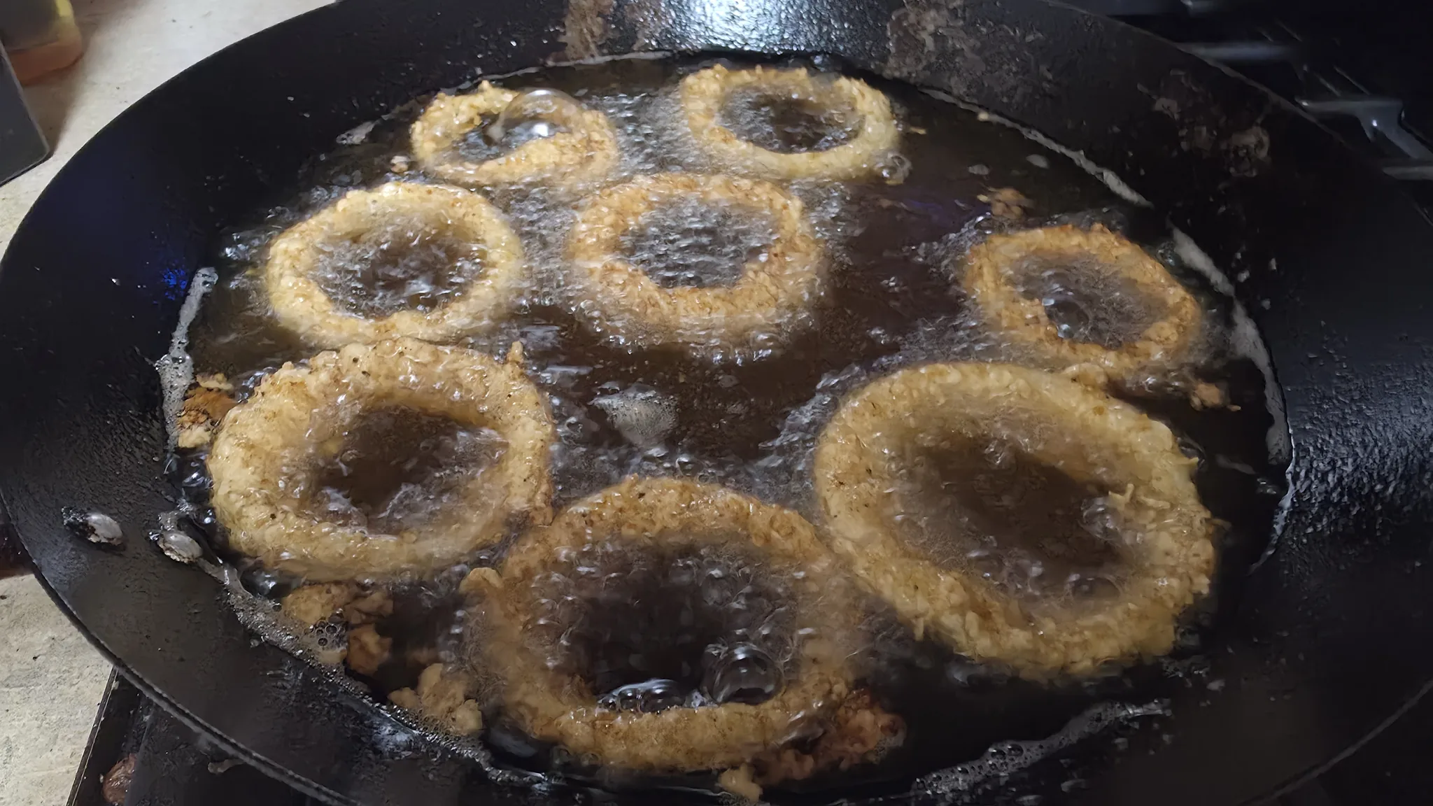 Double-dredged onion rings frying in a cast-iron pan