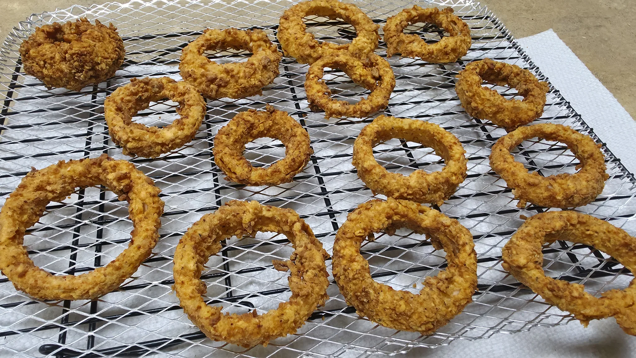First-fried onion rings resting in a single layer on a wire rack